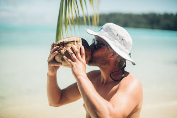 man drinks coconut milk straight from the coconut on a tropical island