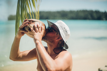 man drinks coconut milk straight from the coconut on a tropical island
