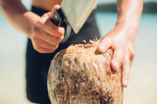 Man cuts open coconut on the beach with a machete
