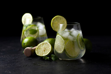 two fresh glasses of non-alcoholic mojito, against a dark background, on a black table, summer cocktails with lime and mint
