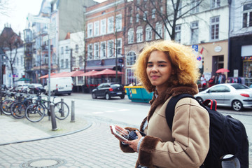 Plakat young pretty african american girl with curly hair making photo on a tablet, lifestyle people concept, tourist in european german city