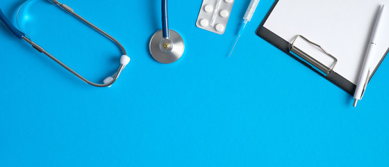Medical equipment on blue background. Top view table with stethoscope, medical clipboard, pills and syringe. Medical banner design with copy space. Healthcare and medical concept.