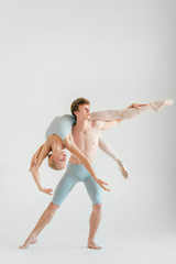 Fototapeta premium Young couple of modern ballet dancers posing over white studio background