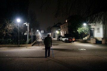 Walking alone silhouette of senior man walking on French street at night using walking stick preserving equilibrium with blue telescopic aluminum cane Medical assistance and rehabilitation