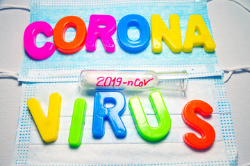 What is Coronavirus, the text is written in plastic letters in different colors on background with protective masks. Glass vial with 2019 nCoV inscription in red felt pen.
