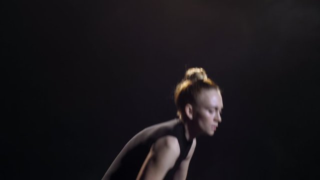 Close-up of graceful female dancer performing energetic impulsive movements of modern contemporary choreography against black background. Young artist emotionally dancing in twilight of studio