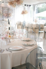 Decor of a wedding luxury dinner in white and pink colors. Served tables with silver and gold objects, plates, glasses and cutlery. Fresh flowers roses in vases.