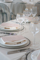 Decor of a wedding luxury dinner in white and pink colors. Served tables with silver and gold objects, plates, glasses and cutlery. Fresh flowers roses in vases.