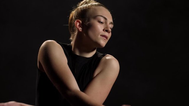Close-up portrait of sensual female artist during spectacular dance performance of contemporary choreography. Young emotional dancer in black leotard expressing soul of dance in twilight of studio