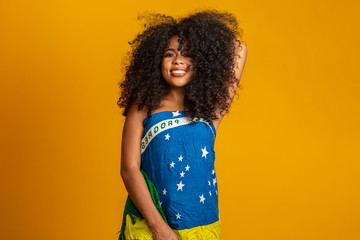 Happy black woman fan holding a Brazilian flag. Brazil colors in background, green, blue and yellow. Elections, soccer or politics.