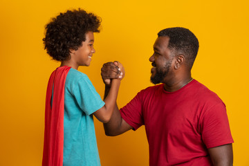 African Father and Son playing Superhero at the day time. People having fun yellow background. Concept of friendly family.