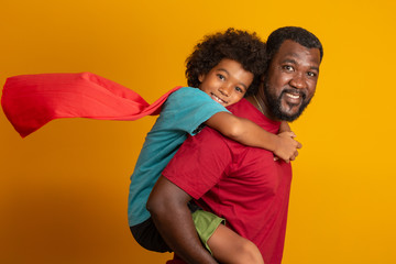 African Father and Son playing Superhero at the day time. People having fun yellow background....