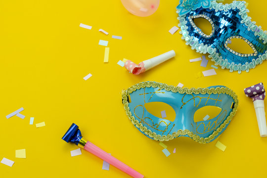Table top view aerial image of beautiful colorful carnival season or photo booth prop Mardi Gras background.Flat lay object blue mask with decorations on yellow wallpaper.Free space for text mock up