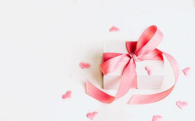 White gift box with pink ribbon and a small pink hearts on white background. Selective focus. Copy space