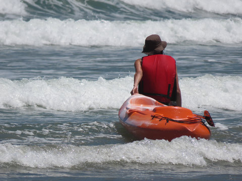 Man with cloth hat carrying kayak on the beach among the waves