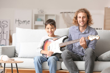 Man and his little son playing guitar at home