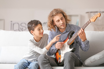 Man and his little son playing guitar at home