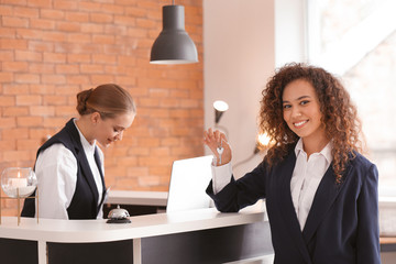 Young woman with key from room at reception desk in hotel
