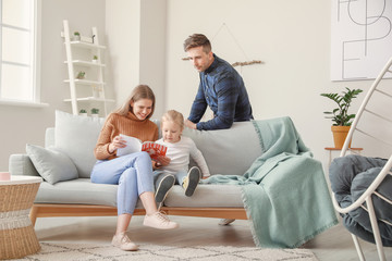Happy young family reading fashion magazine while sitting on sofa at home