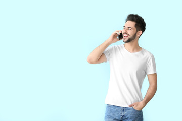Happy young man talking by mobile phone on color background
