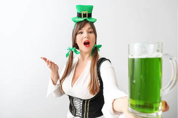 Funny young woman with beer on light background. St. Patrick's Day celebration