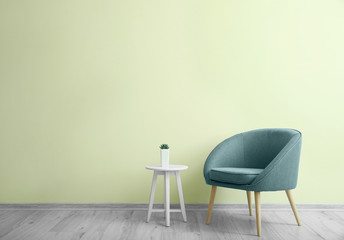 Stylish armchair with table near color wall in room