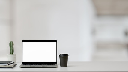 Close up view of workspace with laptop, office supplies, coffee cup and cactus pot on white table with blurred background