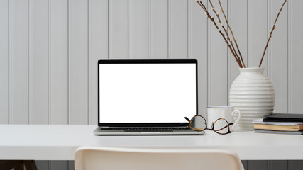 Close up view of workplace with blank screen laptop, office supplies and decoration on white table with plank wall