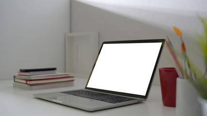 Side view of stylish workspace with blank screen laptop, office supplies and red coffee cup