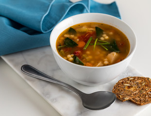 close up of a bowl of homemade chicken vegetable soup with a blue napkin in behind and served with gourmet crackers.