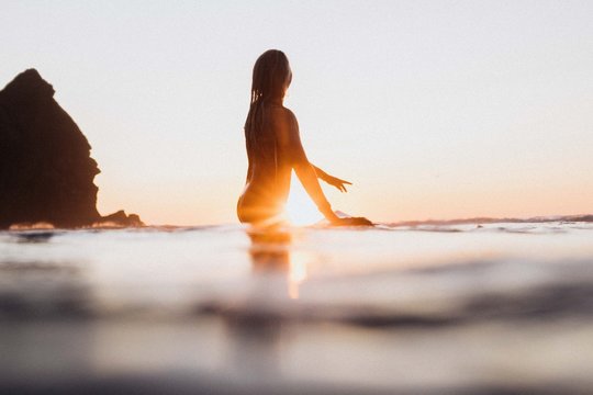 Girl looks out to sea on her surfboard at sunset