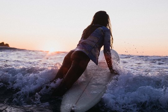 Young girl paddles out on surfboard at sunset
