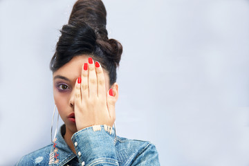 Serious young girl looking with one eye at the camera as she covers the other with her hand in a...