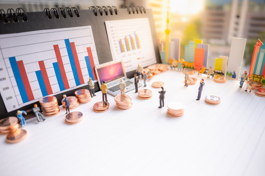 Miniature people: business man standing with stack of coins, lap top, bar graph on blurred city scape and copy space using as background business money investment plan, real estate, property concept.