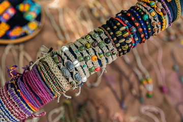Obraz premium Close up of row of colored hand made bracelets in the farmer's Market. Natural and colored strings, beads, small stones. Blurry background.