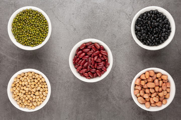 Grains or beans, red bean, black bean, green bean, soybean, peanut in the white bowl placed on the black cement floor. Top view.
