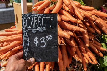 Hand written blackboard sign with the price of bright orange carrots at the farmer's market. Real,...