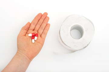 Female hand with pills and roll of toilet paper on white background, concept of diarrhea or...