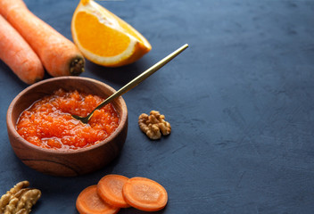 Vegetable carrot jam in a wooden bowl on a dark blue background, a place for text