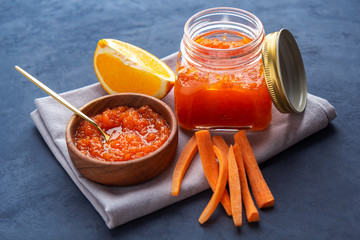 Carrot jam in a jar and a wooden bowl against a dark background