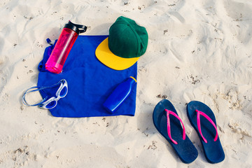 vacation and summer holidays concept - flip flops, towel, cap, bottled water and bottle of...
