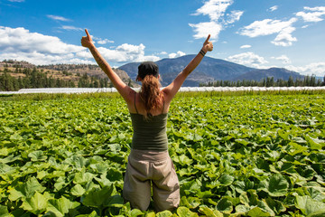 A happy caucasian girl is viewed from the rear as she raises her arms in the air with thumbs up,...