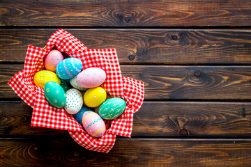 Basket with painted eggs for Easter dinner on dark wooden desk top-down copy space