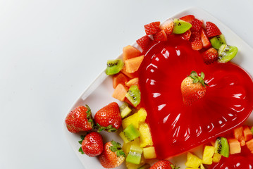 Heart shape strawberry gelatin decorated with fresh strawberry, kiwi and pineapple. Dessert for couple.