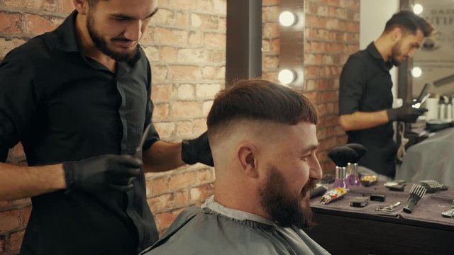 Male stylist taking barber scissors for male cutting in beauty salon. Hipster man receiving stylish haircut in barber shop. Barber shaving male hair with electrical razor