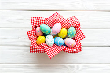Easter eggs painted in basket on white wooden desk top-down copy space