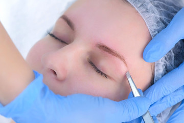 Obraz na płótnie Canvas Cosmetologist plucks out hair on eyebrows with tweezers for woman, face closeup. Eyebrows tweezing procedure. Beautician is making brows correction with cosmetic tweezer. Beauty industry.