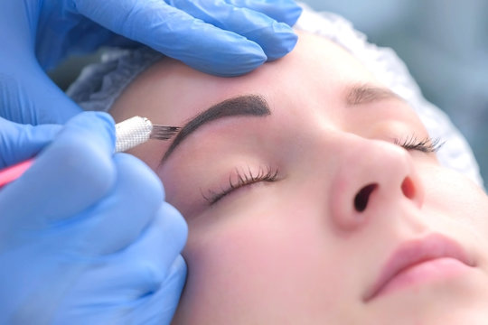 Beautician is painting shaping contour using manual tool for tattoo, woman's face closeup. Cosmetologist making eyebrows microblading procedure in beauty salon for girl. Beauty industry concept.
