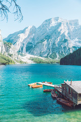 view of wooden house on water with pier and boats lake in dolomites mountains