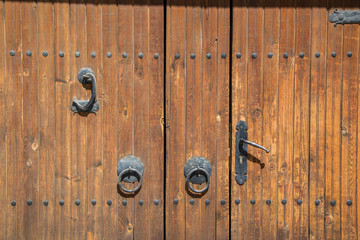 Old brown wooden massive gate, closed door, double entrance with handmade iron handles and knockers